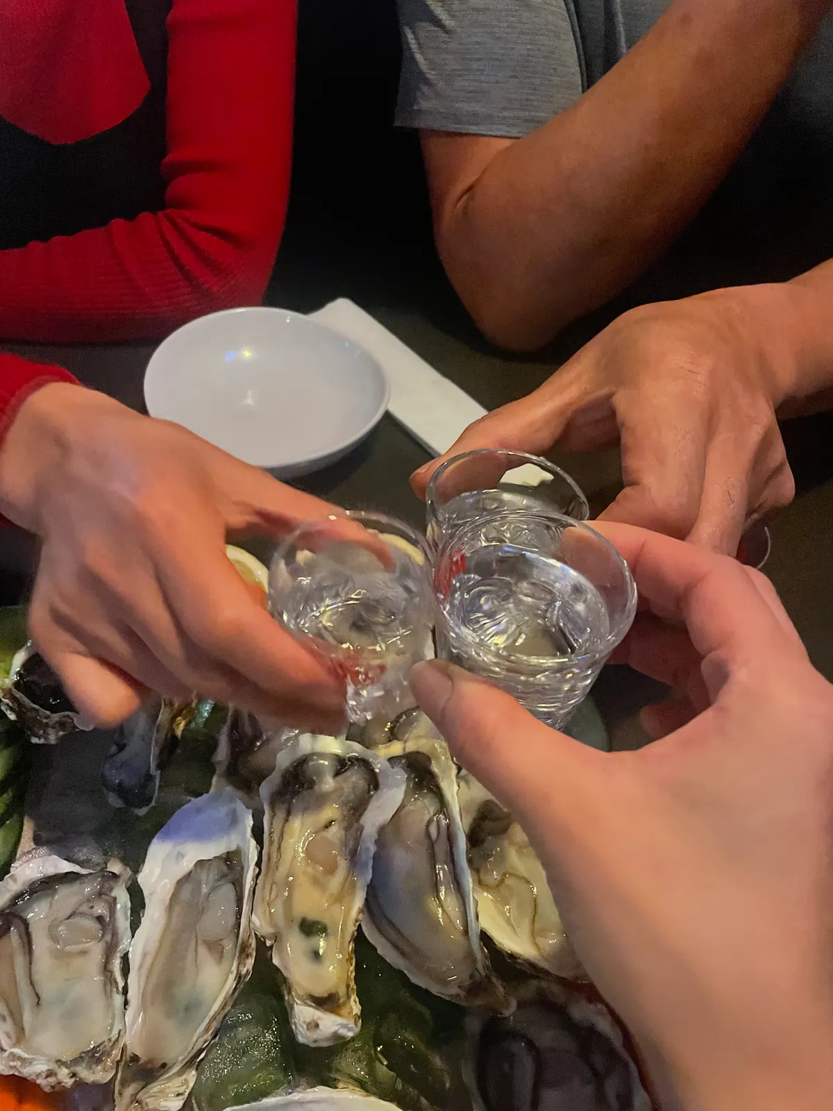 Guests toasting soju over a platter of fresh oysters